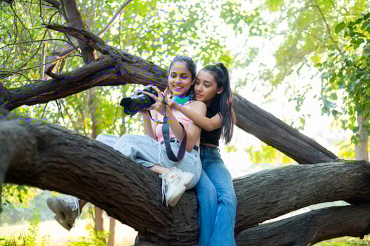 Women Friends Sitting On Branch Tree While Checking DSLR Camera photo