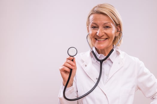 Portrait of mature female doctor with stethoscope on gray background. photo