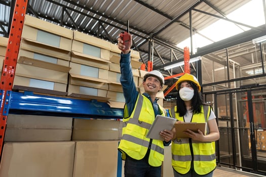 Two smile warehouse workers in uniforms and yellow helmets on heads standing and talking about job. adviser photo