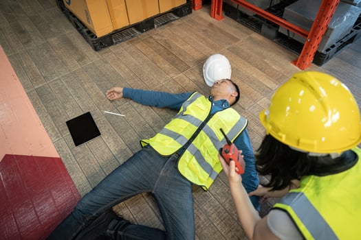 A female warehouse worker using a walkie-talkie called the factory's first aid team to rescue an unconscious man. pass out or blackout, unsafe, emergency photo
