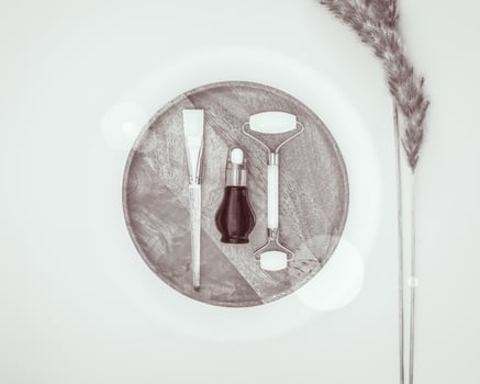 A bottle of serum and cosmetic accessories on a wooden plate with dried flowers and sun glare photo