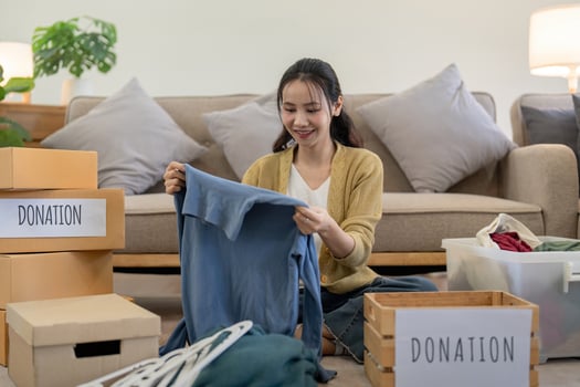 Woman asian holding donation box full with clothes and select clothes. Concept of donation and clothes recycling. Helping poor people photo