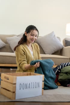 Woman asian holding donation box full with clothes and select clothes. Concept of donation and clothes recycling. Helping poor people photo