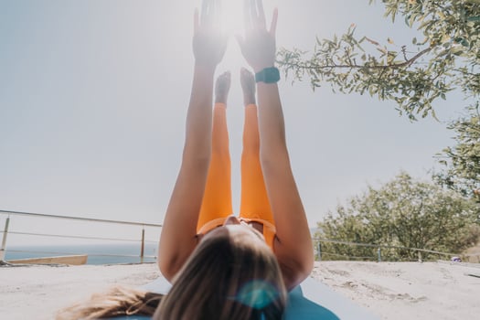 Fitness woman sea. Happy middle aged woman in orange sportswear exercises morning outdoors on yoga mat with laptop in park over ocean beach. Female fitness pilates yoga routine. Healthy lifestyle. photo