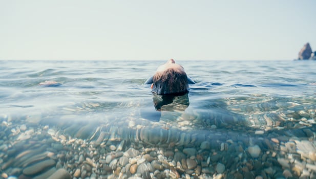 Woman swimming in sea at sunset, float on calm water back view. Concept of body image and fitness, enjoying a serene beach. Happy woman with perfect fit body enjoys sea beach photo