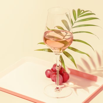 Glass of rose wine with palm leaf and grape on a pink background photo