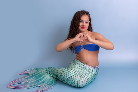 A pretty child girl in a mermaid costume, sitting on a blue background photo