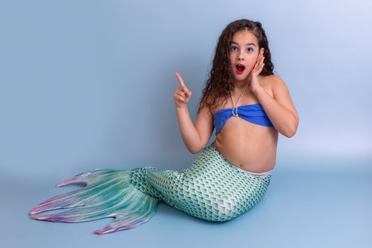 A surprised girl in a mermaid costume sits on a blue background photo