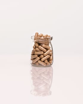 Organic herb capsules in a glass bottle on a white table with reflection photo
