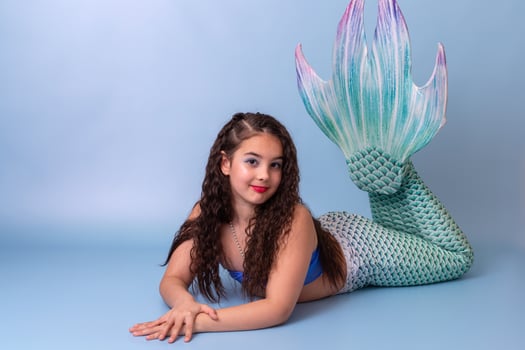 A pretty child girl in a mermaid costume lie isolated on light-blue background photo