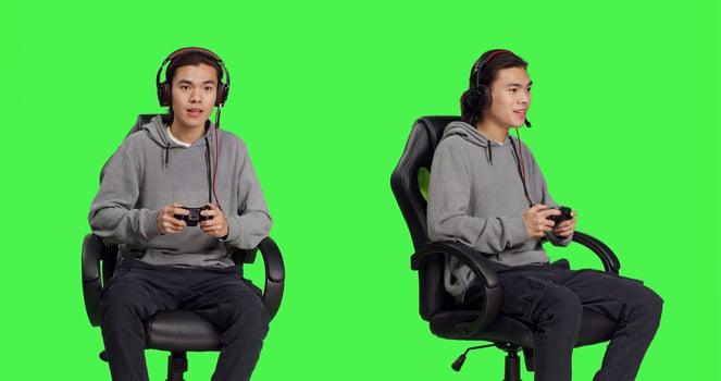 Confident guy playing games in studio, having fun with friends on online gaming quest over greenscreen backdrop. Asian man gamer enjoying rpg competition sitting on chair. photo