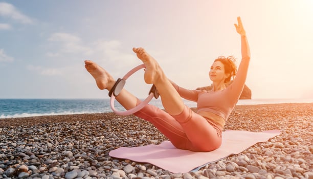 Woman sea pilates. Sporty happy middle aged woman practicing fitness on beach near sea, smiling active female training with ring on yoga mat outside, enjoying healthy lifestyle, harmony and meditation photo
