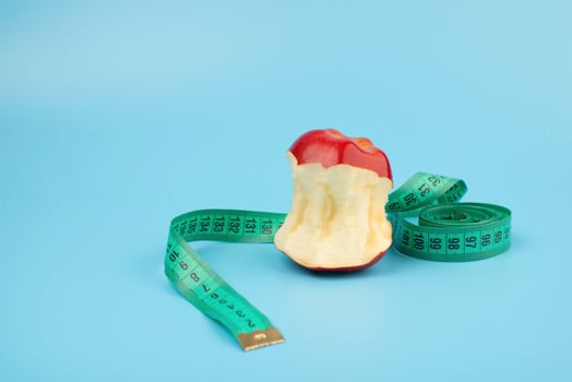 Red bitten apple and measuring tape on a blue background with copy space. photo