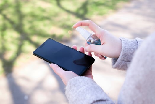 Close up female hand holding smartphone and cleaning spray on her smartphone. Good personal hygiene practices on the street photo