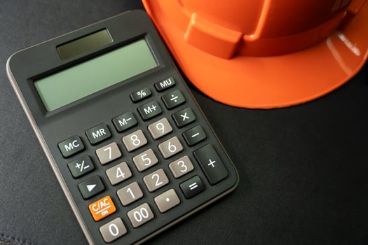 Calculator and Orange safety helmet or hard hat on black background. Business building idea or engineering context. photo