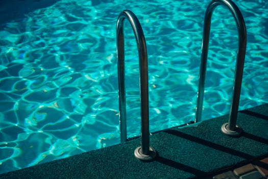 A metal ladder is in the water. The water is clear and calm. The ladder is in the middle of the pool. photo