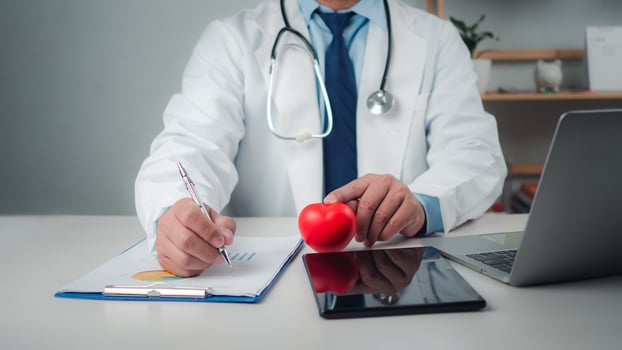 Doctor showing a red heart at hospital office, Healthcare worker and doctor service, Digital laptop in modern office, Medical technology concept, Health insurance concept, Health planning concept. photo