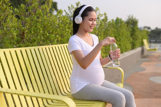 Beautiful pregnant woman drinking bottle of pure water in the park, Healthy and active pregnancy lifestyle concept. photo