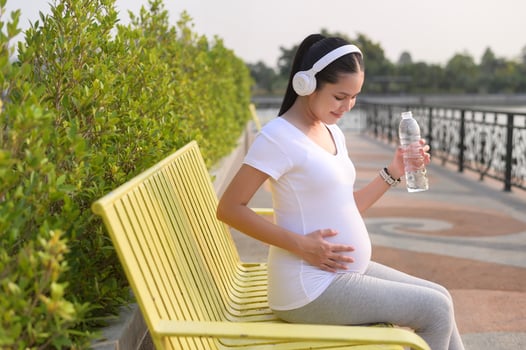Beautiful pregnant woman drinking bottle of pure water in the park, Healthy and active pregnancy lifestyle concept. photo