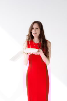 Beautiful and young girl with long hair in a red dress blows out a candle on a bento cake at a party photo