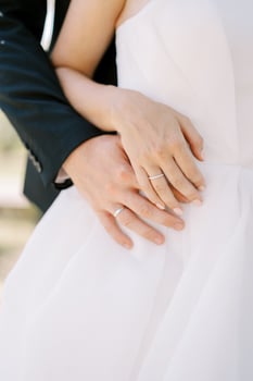 Groom hugs bride from behind, placing her hand on his hand. Cropped. Faceless photo