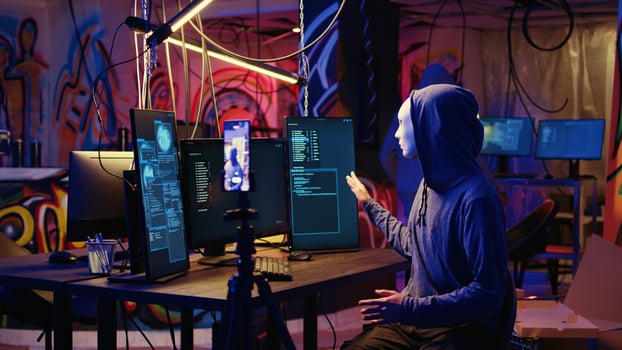 Hackers concealing their identity filming ransom in hidden underground base, threatening to release stolen data publicly if payout demands are not met, using phone to record blackmail footage photo