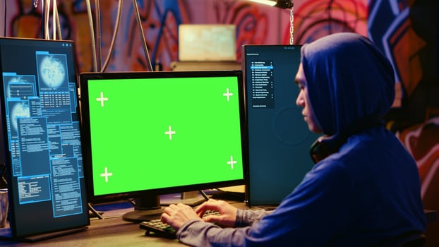 Asian hacker in hidden place with graffiti walls using green screen computer to deploy malware on unsecured devices, stealing sensitive data from unaware users online and selling it on black market photo