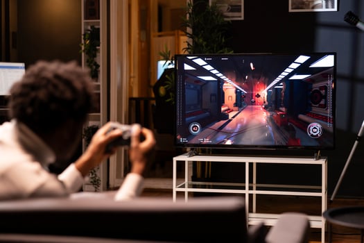 Gamer using controller to play first person shooter videogame on smart TV, shooting robotic enemies. African american man in home theatre using high tech gaming console gamepad photo