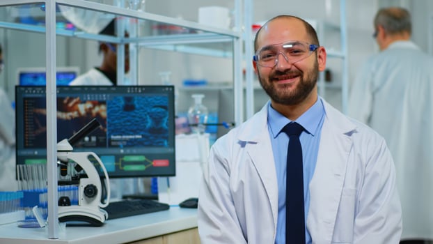 Microbiologist sitting in laboratory looking at camera in modern equipped lab. Multiethnic team examining virus evolution using high tech and chemistry tools for scientific research, vaccine development. photo