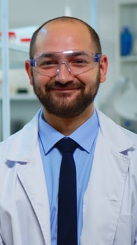 Portrait of scientist man smiling at camera sitting in modern equipped laboratory. Multiethnic team examining virus evolution using high tech and chemistry tools for scientific research, vaccine development. photo
