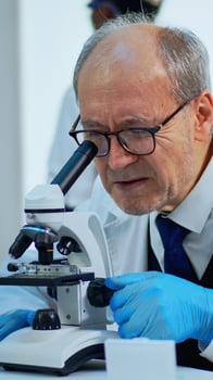 Laboratory scientist conducting experiment looking at microscope in busy modern lab. Eldery man working with various bacteria tissue, blood samples, concept of pharmaceutical research for antibiotics photo
