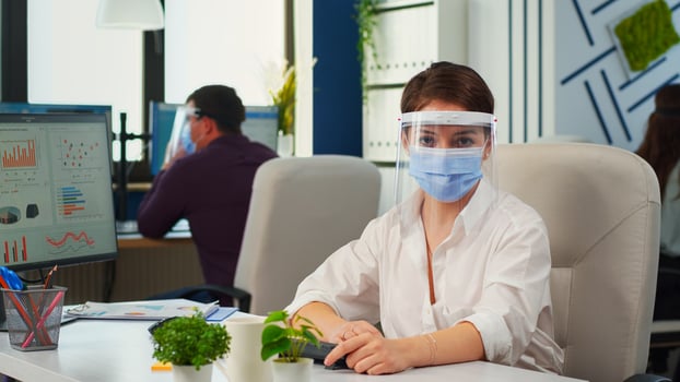 Businesswoman with visor and mask talking in front of camera having call with partners. Pov of manager speaking with remotely team during online conference while colleagues working in background photo