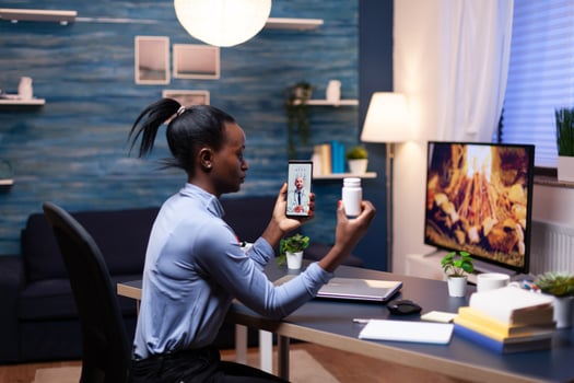 Doctor explaining treatment to dark skinned woman during call late at night while she's holding pills bottle. Black patient in a call with medic discussing health problems of woman. photo