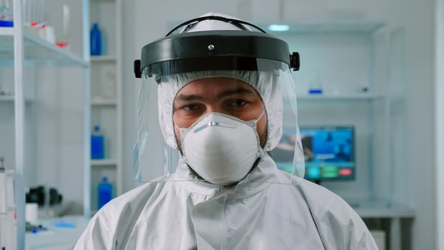 Portrait of chemist doctor looking up at camera sitting in modern equipped lab wearing protection suit. Examining virus evolution using high tech and chemistry tools for vaccine development. photo