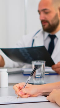 Close up of nurse taking notes on clipboard while radiologist coworkers discussing in background analysing x-ray and writing on laptop. Profesional teamworkers having medical meeting, brainstorming photo