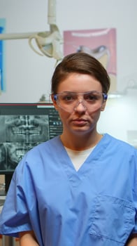 Dental assistant explaining to patients the importance of oral hygiene looking at camera in dental center while doctor is working with patient in background. Stomatologist nurse speaking on webcam photo