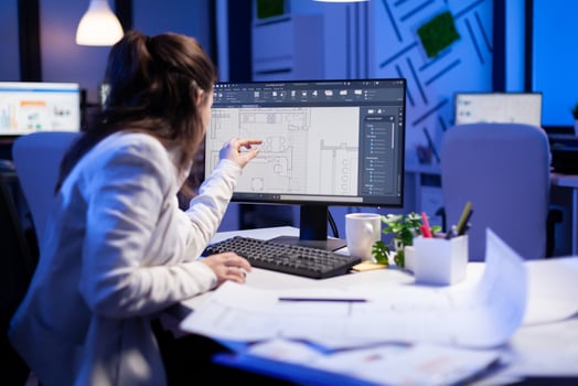 Over the shoulder shot of engineer woman drawing architectural plans and looking at cad software on desktop computer. Designer using arhitecture blueprints of buildings creating industrial prototype photo