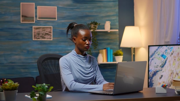 African young business woman coming at home workplace late night. Black entrepreneur working in moder living room overtime writing on keyboard looking at desktop respecting deadline of project. photo