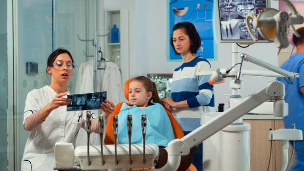 Pediatric woman dentist treating little girl patient in modern stomatological dentistry office showing teeth x-ray explaining to mother dental intervention. Visiting dentist with children. photo