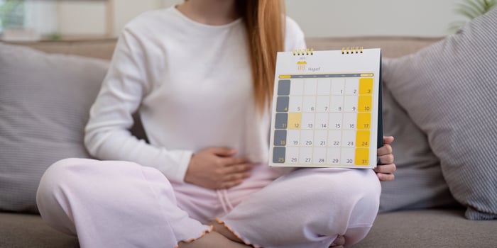 Woman sitting with a calendar and holding her stomach. Concept of menstrual cycle tracking and health photo