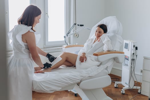 Beautician depilating young woman's legs with liquid sugar in spa center photo