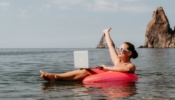 Woman freelancer works on laptop swimming in sea on pink inflatable ring. Happy tourist in sunglasses floating on inflatable donut and working on laptop computer in calm ocean. Remote working anywhere photo