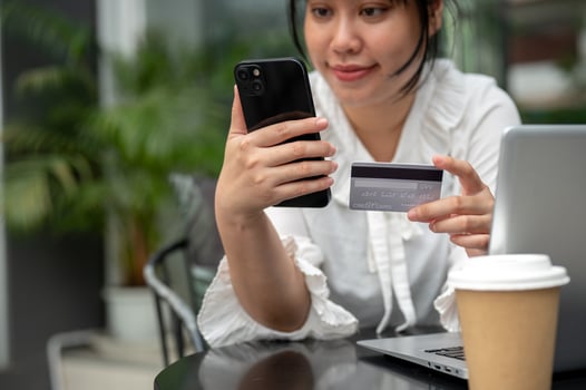 A young Asian woman holding a credit card and her smartphone while sitting at a table outdoors. photo