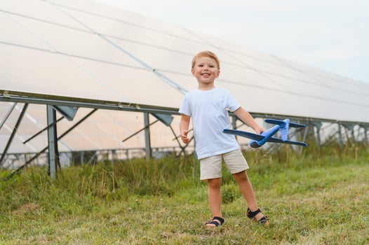 Little happy boy playing with toy airplane near solar panels. photo
