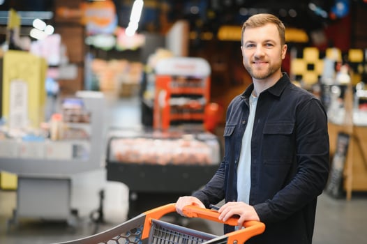 Young man buying groceries at the supermarket. Other customers in background. Consumerism concept. photo