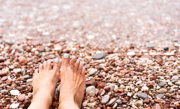 Woman's feet on a pebble beach on the sea. Vacation and travel concept. Rest, relaxation, sunbathing. Close-up. Copy space. Selective focus. photo