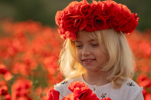 A young girl wearing a red flower crown stands in a field of red flowers. She is smiling and she is enjoying the beautiful scenery. photo