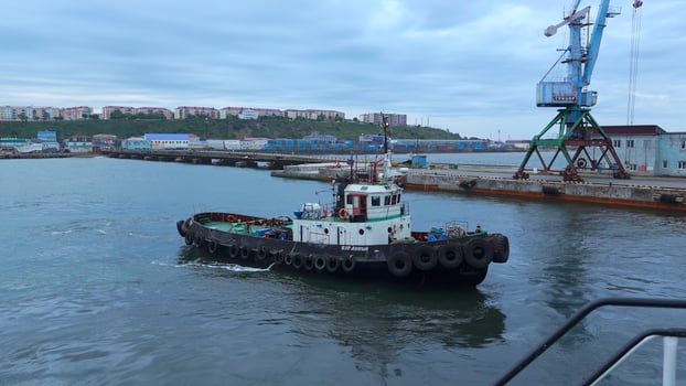 Fishing boat on background of port in cloudy weather. Clip. Fishing vessel sails out of seaport into sea. Fishing boat sails into sea on cloudy day photo