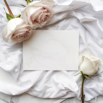 Elegant blank white card surrounded by white and pale pink roses on a crumpled white silk fabric for romantic message or invitation. photo