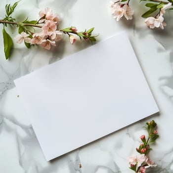 Blank white greeting card with cherry blossoms on marble background, perfect for spring celebrations or special occasions. photo
